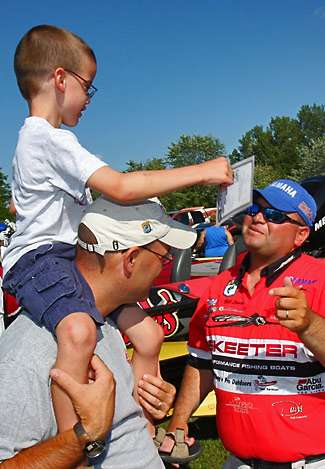Bill Lowen signs an autograph card and hands it to Alex Roberts while his dad Chuck Roberts gives him one of the best views of Angler Alley.