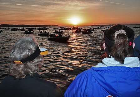 Fans watch the anglers in the staging area as the sun rises above the horizon.