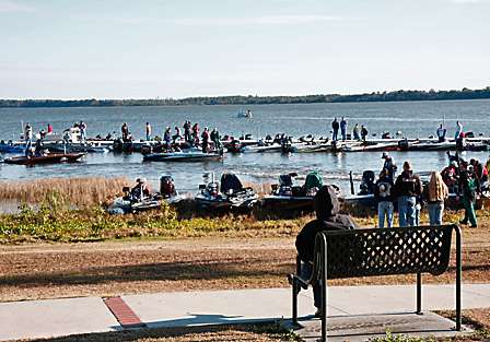 A lady sits on a bench in Wooten Park and watches as the competitors come and go on the docks before her.