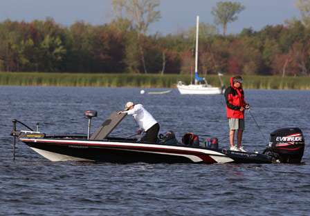 Pro Mike Smith grabs a rod from the rod locker as his co-angler Rick Sweadner works a bait through shallow grass.