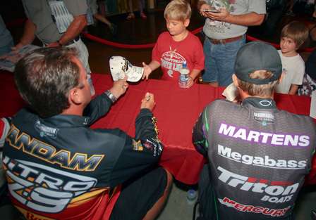 Kevin VanDam and Aaron Martens sign caps for two young fishing fans. 