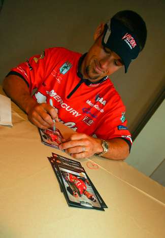 John Crews autographs a set of cards with a photo of him holding one of his best fish caught during his win this year on the California Delta. 