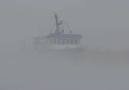A transport boat, which delivers supplies to offshore oil rigs, is barely visible through the fog.