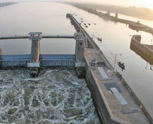<p>
	A muddy water spills through the dam, anglers idle into the lock on the right.</p>
