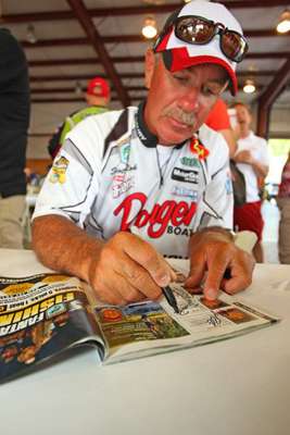 <p>
	Scott Rook signs his autograph on his picture in a magazine.</p>
