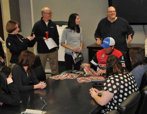 <p>Employees gather around as Pace signs copies of the <em>Bassmaster</em> cover for staff members.</p>
