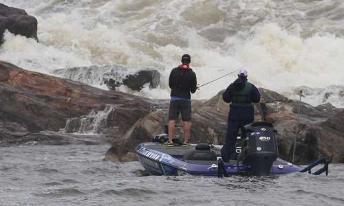 The turbulent waters create an imposing scene with an angler standing in front of it.