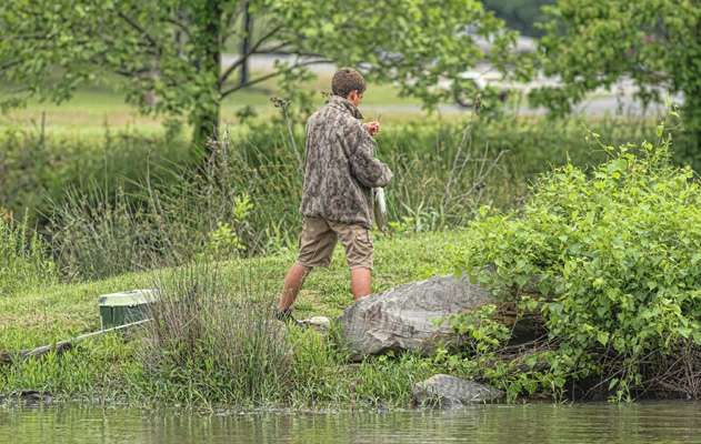 A young angler across the creek, lands a fish and turns his back to unhook it.