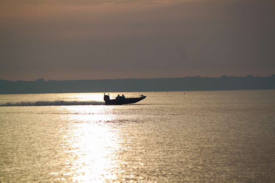 An angler runs down the lake as the sunrise shines down.