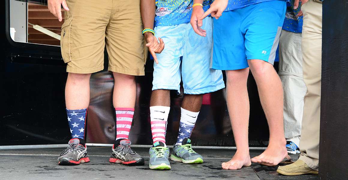 22.	Jon Stewart (left) is wearing the socks Goodson gave him yesterday. They compared their Day 2 footwear. Goodson (middle) is rocking his socks, Younginer (right) is sporting his flip-flop look and Tournament Director Hank Weldon (far right) shows off his kicks too.