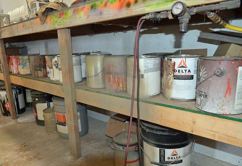 Below his bench are bulk gallon cans of paint.