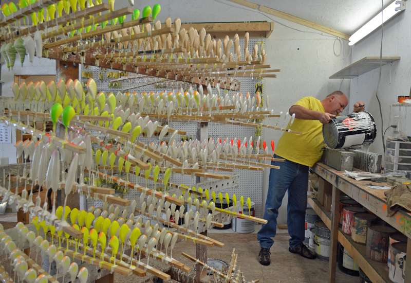In his shop at any one time you might see as many as several hundred balsa baits in various forms of completion. Here he's filling a tank with primer while some partially finished baits dry on racks.