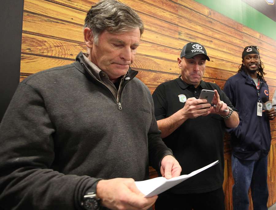 Tommy Sanders takes a quick look at his notes for the next live segment. In the center is B.A.S.S. emceeâ¦possibly updating his Facebook status? On the right is the guest about to step to the podium, Willie Young, defensive end for the Chicago Bears.