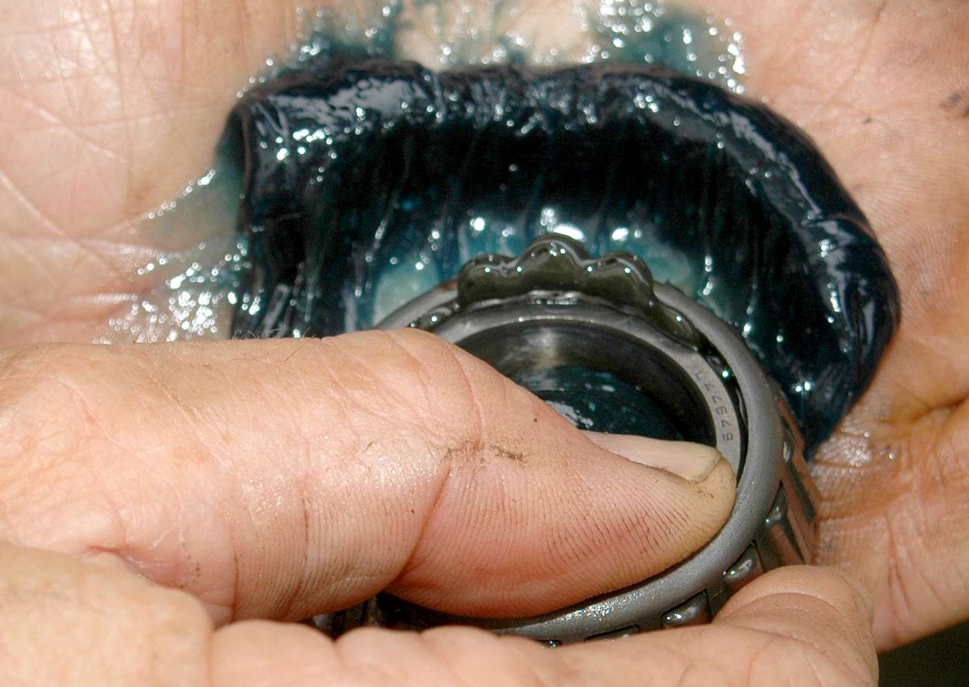 Repeatedly push the wide edge of the bearing through the edge of the grease and forcefully slide it across your palm. This will push new grease into the bearing and flush the old grease out. Wipe away the old grease, rotate the bearing and repeat until you come full circle.