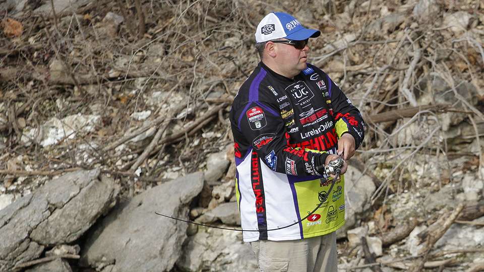 As he runs out of docks he picks up a spinnerbait and throws it parallel to a rocky bluff bank.