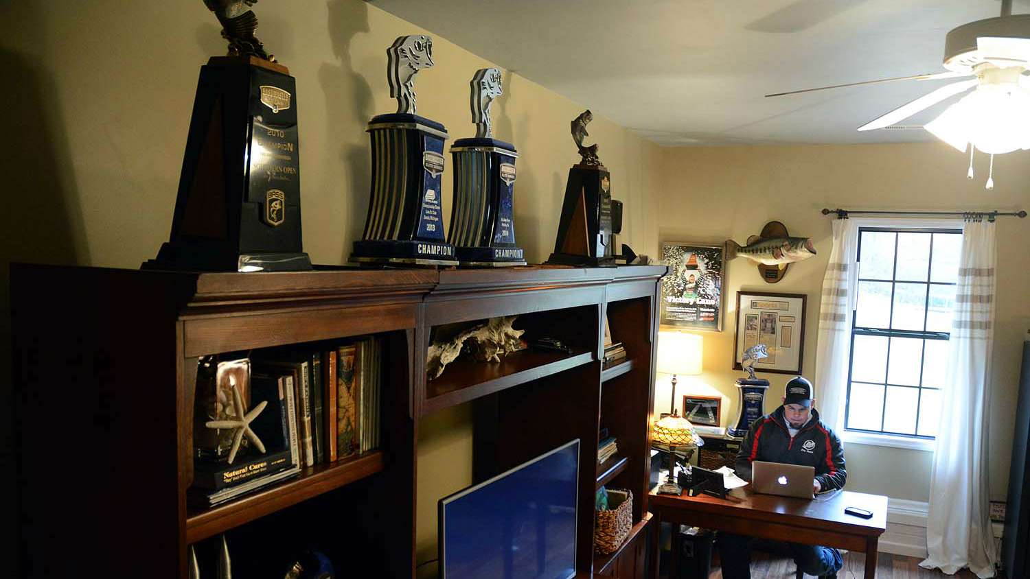The business side of the sport happens in this home office. Behind Lane is the winnerâs trophy from the 2015 Elite Series on the Sabine River. Flanking the top shelf are trophies from Bassmaster Open wins at Lake Okeechobee (2010) and The Harris Chain (2012). In between are trophies from Elite Series wins at Lake St. Clair (2013) and the St. Johns River (2014). 