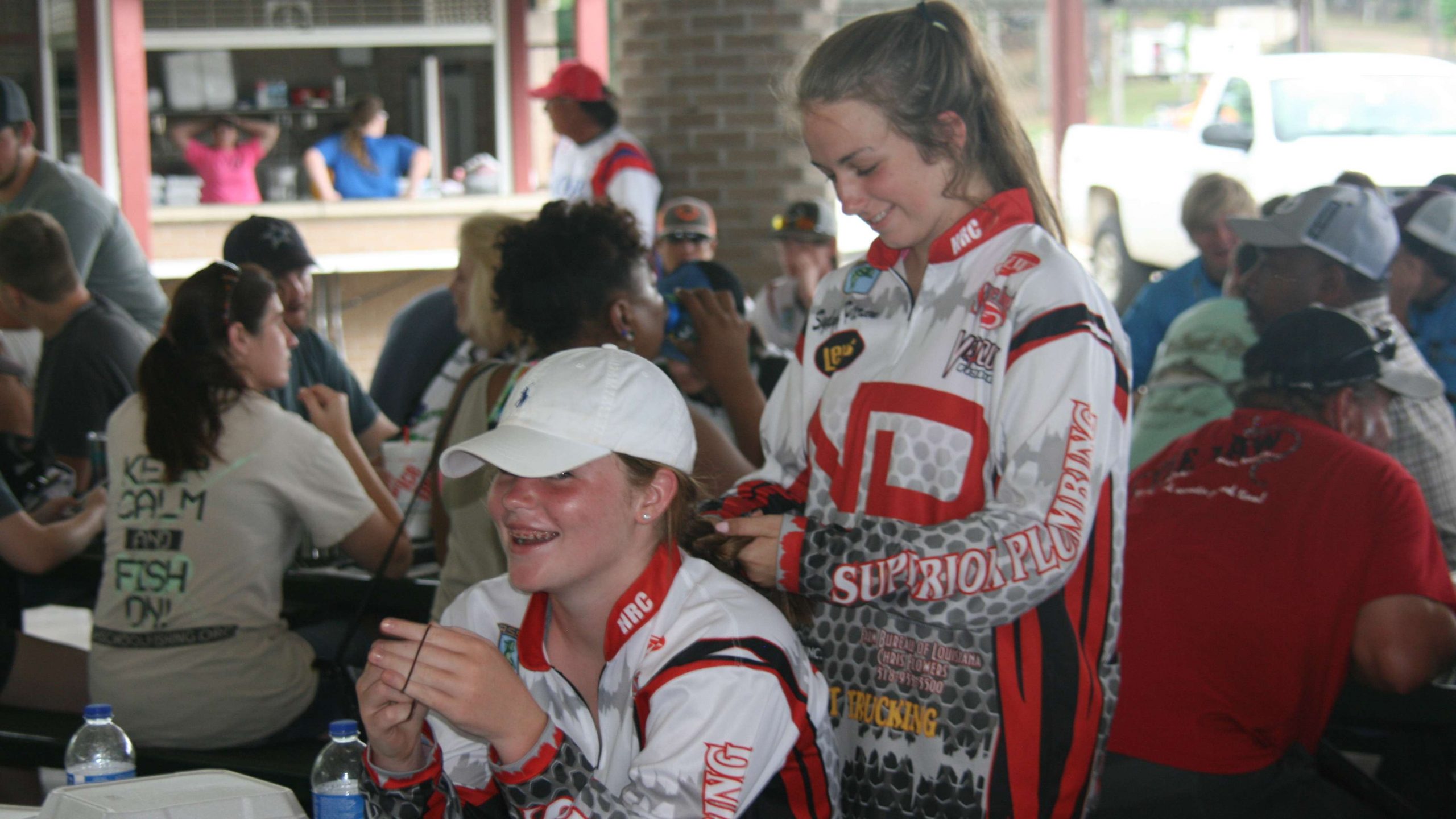 Erin Meeks has her hair braided by Sydney Peterson, both of North DeSoto (Louisiana) High School, as they await tournament director Hank Weldon to take the stage for the anglers' meeting.
