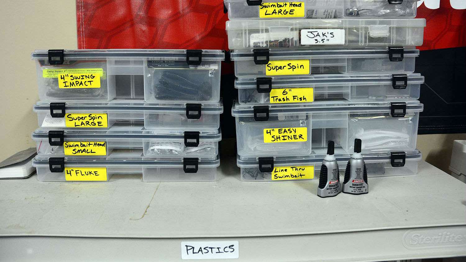 Swimbaits and related terminal tackle is stored in boxes with the yellow labels. Nearby are bottles of Loctite glue for permanently securing soft plastics to the jig heads.