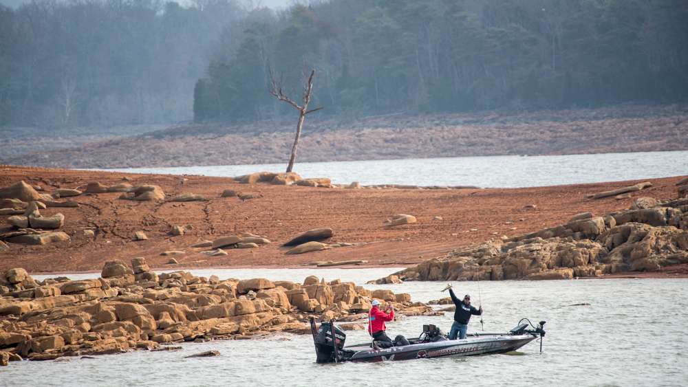 Mullins lets out a loud yell and holds the fish up high above his head. 