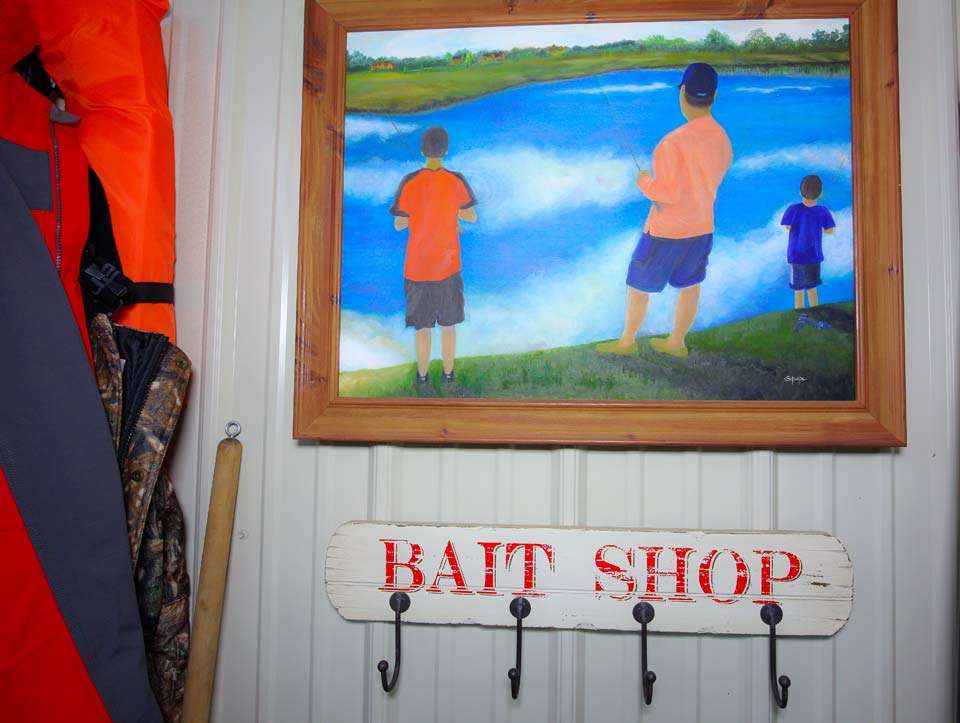 Near the door is a painting of a father and two sons fishing and an unused coat rack. 