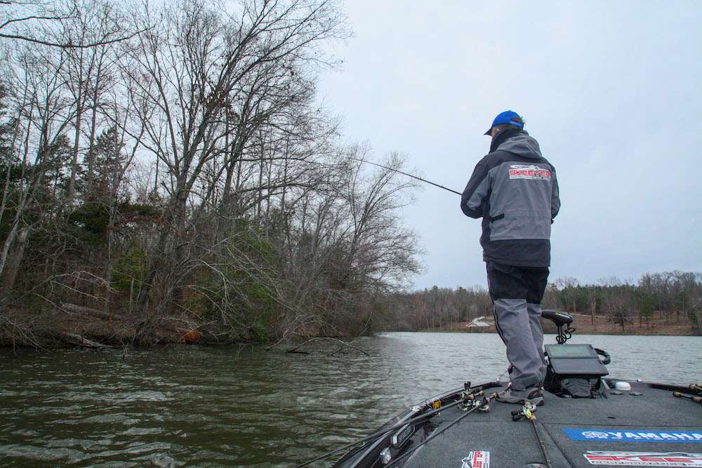 It was a real honor for us when Jay Yelas accepted his second Day on the Lake challenge, this one on March 9, 2020, at hyper-obscure Lake E. As youâre about to discover, Yelas can still summon up the mojo required to score a bodacious bag of bass!
<br><br>
<b>6:48 a.m.</b> Itâs 56 degrees, damp and windy when Yelas and I arrive at Lake E. âItâs supposed to be cloudy all day with rain late this afternoon,â he says as he pulls an arsenal of Lewâs rods and reels from storage and fans them across the deck of his boat. âMoving baits like crankbaits and spinnerbaits should work, but âbite windowsâ are typical in early March, so Iâll probably have to go to a jig when the action tapers off.â <br><br>

<b>7 HOURS LEFT</B><BR>
<b>7:15 a.m.</b> We launch the Skeeter. Yelas checks the water temp: 52 degrees. âThis is a tricky time of year to fish because bass are starting to move up shallow from their deep winter haunts, but with the spawn still a month away, theyâre probably not locked into skinny water yet. Theyâll often âstageâ around isolated wood, rock and grass cover near potential spawning areas and will fatten up prior to going on bed. âI want to run the lake for a few minutes and see what cover and structure options are available.â<br>
<b>7:34 a.m.</b> After some exploratory cruising, Yelas drops his trolling motor near a main-lake point in Lake Eâs upper end and makes his first casts of the day with a chartreuse shad Lucky Craft 2.5 squarebill crankbait. âA small squarebill is a good choice in early spring; it deflects off cover and resembles a crawfish, which are shallower and more readily available to bass now than baitfish like shad. Biologists also tell me that [crawfish] are a great source of calcium, which promotes bass egg sac development.â Wow! Who knew? <br>
<b>7:40 a.m.</b> Yelas switches to a 1/2-ounce red craw XCalibur lipless crankbait and quickly bags his first keeper bass of the day, a 1-pound largemouth. âThis fish was on a patch of gravel on the point. I was using a yo-yo retrieve and it hit on the fall.â <br>
<b>7:46 a.m.</b> Another bass pops the lipless crankbait but doesnât hook up. <br>
<b>7:52 a.m.</b> Yelas tries a 6-inch plum/emerald flake Yamamoto Senko on the gravel patch. <br>
<b>7:59 a.m.</b> He cranks a red craw Strike King 1.5 squarebill across the point. âYou shouldnât have to use a finesse approach in these cloudy, windy conditions to catch fish. They should hit a moving bait.â <br>
<b>8:04 a.m.</b> Yelas slow rolls a 1/2-ounce chartreuse and white MGC spinnerbait across the point. âSpinnerbaits are a good choice in choppy water; they put off a realistic diffused flash.â <br>
<b>8:08 a.m.</b> The point transitions to a steep channel bank with multiple blowdowns. Yelas tries the spinnerbait and 1.5 here without success. <br>
<b>8:11 a.m.</b> Yelas moves to a nearby tributary arm where he casts the lipless crank around a dock.
<br><br>
<b>6 HOURS LEFT</B><BR>
<b>8:15 a.m.</b> Yelas dredges the red squarebill down a submerged tree on a secondary point and bags keeper No. 2, 1 pound, 4 ounces. âThis fish was parked halfway down that sunken tree.â<br>
<b>8:17 a.m.</b> Yelas casts a 1/2-ounce black and blue MGC jig with a matching Yamamoto Flappinâ Hog trailer and swings aboard keeper No. 3, 2 pounds, 12 ounces. âIt hit bottom, I twitched it one time, and she popped it! This is a textbook early spring staging spot: an isolated tree on a point near the entrance to a spawning cove.â <br>
<b>8:20 a.m.</b> Yelas moves to a series of docks where he tries a 3/8-ounce black and blue Z-Man ChatterBait bladed jig with a matching Yamamoto Zako trailer. <br>
<b>8:27 a.m.</b> Heâs probed three docks with the jig and his crankbait arsenal. No takers here. <br>
<b>8:30 a.m.</b> Yelas cranks the ChatterBait around a seawall. âTheyâll spawn against these vertical walls.â <br>
<b>8:36 a.m.</b> He pitches the jig around a series of laydowns. âOften the more wood cover there is close together, the less bass like it. Isolated wood is usually better, especially in early spring.â <br>
<b>8:42 a.m.</b> Yelas is moving rapidly down the bank while making short casts with the red squarebill. âI was in a bite window a half-hour ago, but it may be closing!â <br>
<b>8:50 a.m.</b> Yelas moves straight across the lake to a point with a solitary laydown and tries a white 3/8-ounce MGC swim jig with a matching Strike King Rage Craw trailer, shaking the rod tip during the retrieve âto activate the skirt and trailer.â <br>
<b>8:54 a.m.</b> He casts the jig to the tree. âMake sure you stay well off these big laydowns; they often run out a long distance from shore, and if you bump a branch with your boat, itâll spook the fish.â <br>
<b>9:01 a.m.</b> Yelas zips downlake a quarter-mile to a point at a cove entrance, where he tries the Lucky Craft squarebill. <br>
<b>9:04 a.m.</b> He moves into the cove and casts the lipless crank around a cluster of submerged stumps. <br>
<b>9:09 a.m.</b> Yelas rakes the red 1.5 over a secondary point.