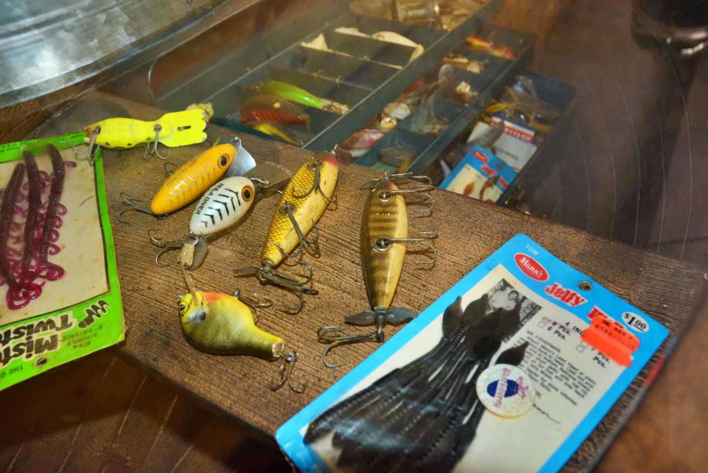 A package of Mannâs Jelly Worms, still in the package, with the photo of Tom Mann on the card. And another unopened package of Mister Twister Centipede Worms is nearby. Between them are vintage hard baits, including an Arbogast Hula Diver.