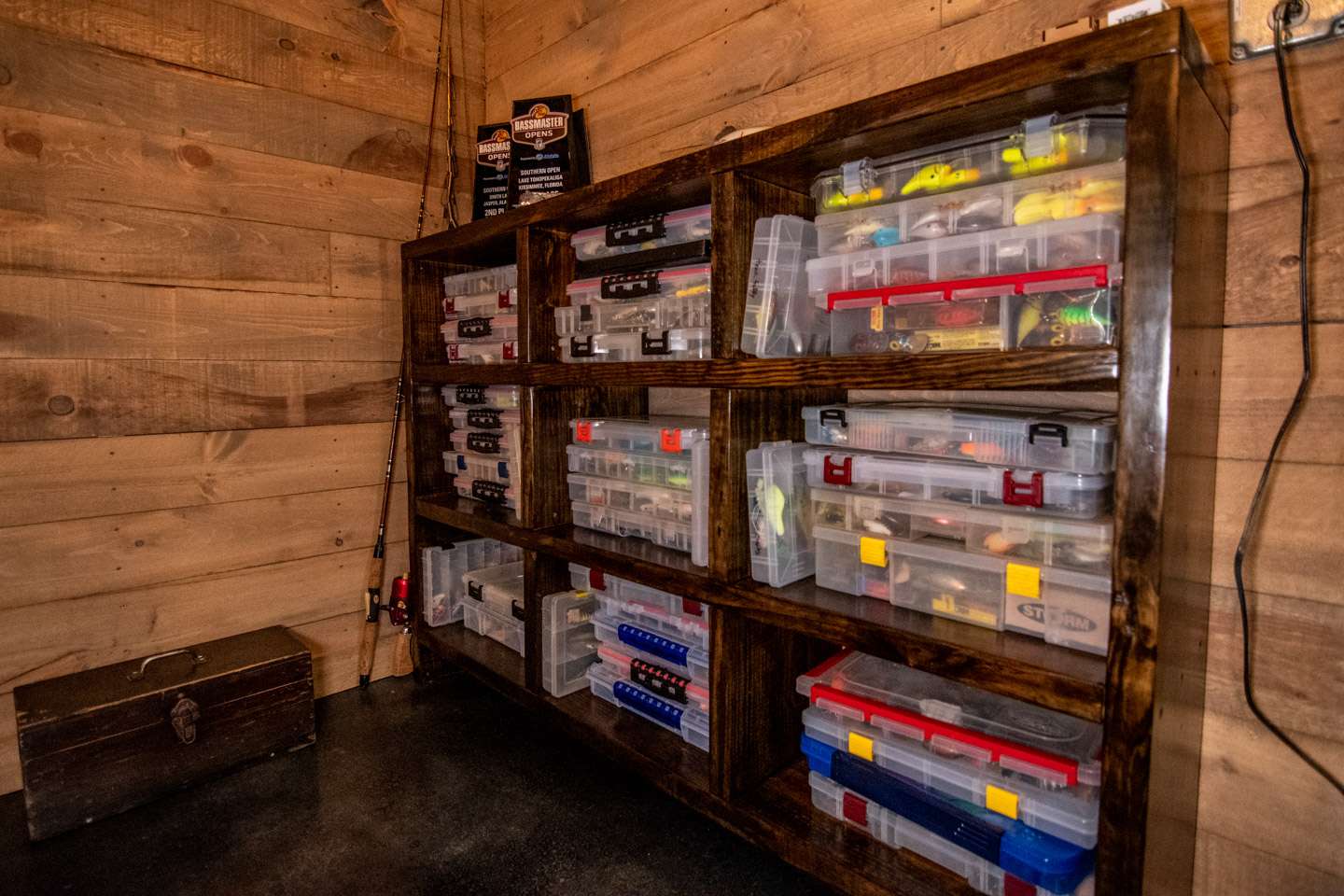 A bookshelf sitting next to the glass case is stocked with tackleboxes filled with more crankbaits and top water lures.  