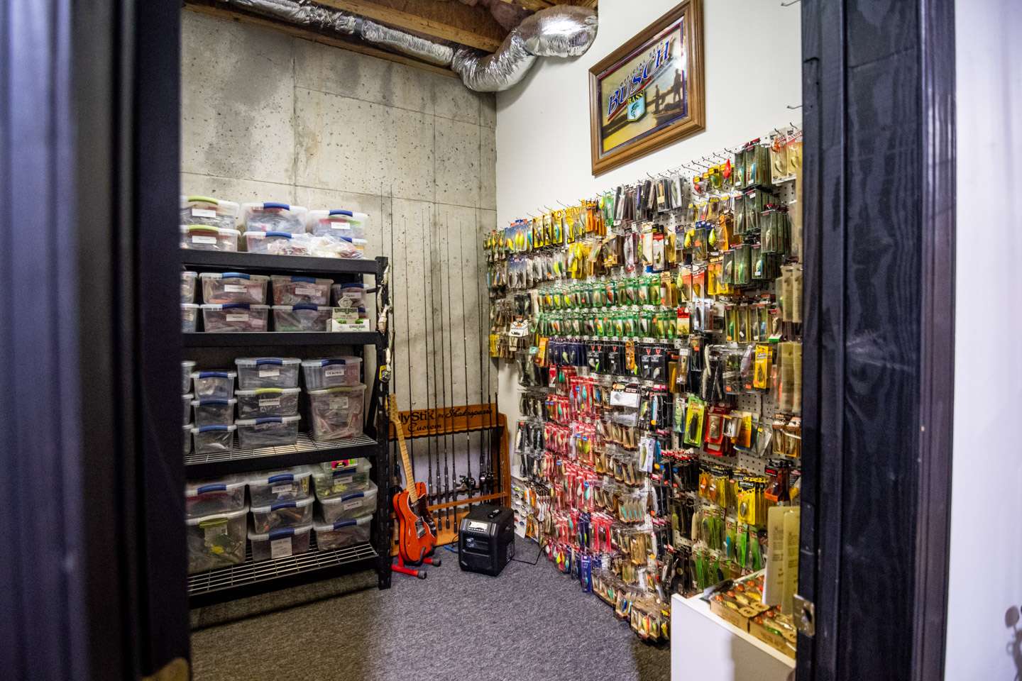 The back of the garage on the right opens into the tournament tackle storage room. This room is organized with pegboards for hanging lure packages and metal shelves for stacking boxes of tackle.