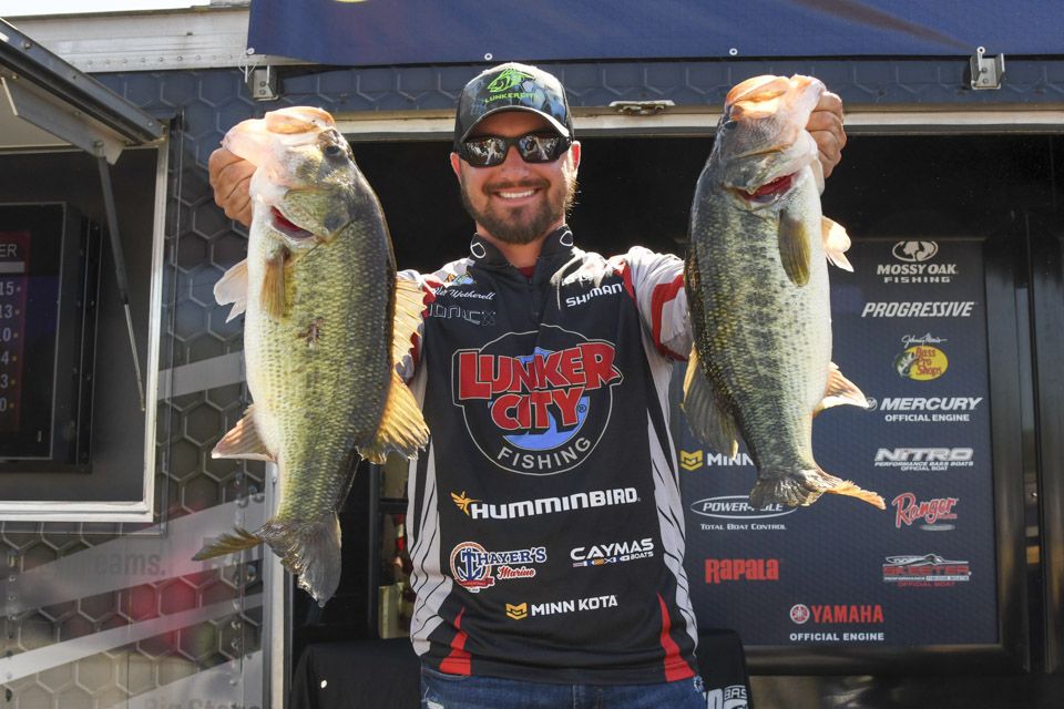 Angler Alex Wetherell holds up two largemouth bass on the weigh-in stage